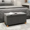 A gray storage ottoman sits in front of a bed in a bedroom. Anteprima dell’immagine prodotto