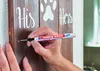 A person's hand is using a marker pen to write on a wooden board with painted text and a paw print. Produktbild-Vorschau