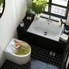 A modern bathroom with a toilet featuring a fox-themed seat, a sink with a plant, and black tiled flooring. Produktbild-Vorschau