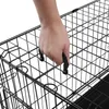 A hand is shown gripping the handle of a black wire dog crate. Produktbild-Vorschau