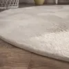 A close-up view of a round, fluffy rug with a subtle pattern, placed on a wooden floor. Produktbild-Vorschau