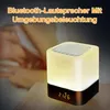 A bedside table with a glowing cube-shaped speaker and clock, with a person's arm in the background. Produktbild-Vorschau