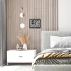 A digital clock and bedside table are shown next to a bed in a bedroom. Produktbild-Vorschau