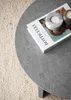 A close-up view of a round coffee table with a book and two candle holders on it, placed on a textured rug. Voir les images du produit