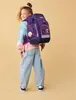 A young girl wearing a backpack and jeans, posing for a photo. Náhled obrázku produktu