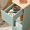 Close-up view of an open drawer of a light green bedside table, with a remote control and decorative paper inside. Náhľad obrázku produktu
