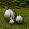 Three brushed stainless steel spheres of varying sizes are placed on a green lawn in a garden setting. Podgląd zdjęcia produktu