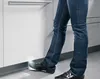 A person's legs and feet are shown in a kitchen environment, interacting with a cabinet. Produktbild-Vorschau