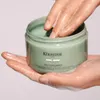 Hands are shown scooping a green clay-like product from a jar. Produktbild-Vorschau