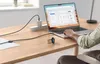 A person is using a laptop on a wooden desk, with a charging cable and a smartwatch visible. Podgląd zdjęcia produktu
