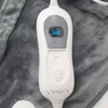 A close-up view of a white electric heating pad controller with a gray display and a slider control, resting on a gray fuzzy blanket. Produktbild-Vorschau