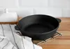A black cast iron pan sits on a metal trivet on a wooden countertop, with a white patterned butter dish and a striped dishtowel in the background. Produktbild-Vorschau