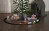 A Christmas train set is arranged around the base of a Christmas tree on a wooden floor. Podgląd zdjęcia produktu