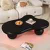 A black cloud-shaped coffee table with a bowl of fruit and a cup of coffee on it, placed in a living room setting with a white sofa and a rug. Voir les images du produit
