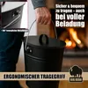 A person is holding a black metal ash bucket in front of a fireplace. Produktbild-Vorschau