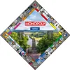A diamond-shaped Monopoly board with a scenic landscape in the center, featuring a river, trees, and a tower. The board spaces are decorated with small images. Produktbild-Vorschau