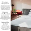 A bedroom scene with a bed, chair, and plants, featuring text overlays describing product features. Produktbild-Vorschau