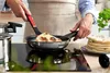 A person is cooking flatbread in a pan on a stovetop. Produktbild-Vorschau