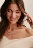 A woman wearing a necklace with a pearl and cross charm. Voir les images du produit