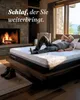 A man is relaxing on a mattress in a cozy room with a fireplace and a large window. Produktbild-Vorschau