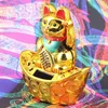 A golden lucky cat figurine sits on a boat-shaped base decorated with coins, against a colorful, abstract background. Produktbild-Vorschau