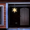 A star-shaped Christmas decoration hangs in front of a brick wall and a white door, with snow on the ground. Náhled obrázku produktu