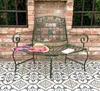 A green metal garden bench with a straw hat and a book on it, placed on a patterned tiled patio in front of a brick wall. Anteprima dell’immagine prodotto
