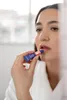 A woman applying lip balm from a tube to her lips. Produktbild-Vorschau