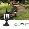 Two black outdoor lamps are placed in a garden setting next to a pathway leading to a wooden house. Produktbild-Vorschau