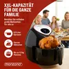 A family is gathered around a table, with a large air fryer prominently displayed in the foreground, showcasing a roasted chicken. Produktbild-Vorschau