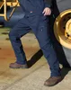 A person wearing work pants and boots leans against a large yellow tire. Anteprima dell’immagine prodotto