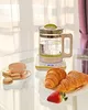 A glass kettle with water on a white base, next to a cup with macarons and croissants with a strawberry on a glass table. Anteprima dell’immagine prodotto