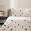 A bed with white bedding featuring a pattern of various dog breeds. Two pillows are visible on the bed, and the duvet cover is spread out. Podgląd zdjęcia produktu