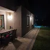A patio area at night with a table and chairs, a walkway, and lawn. Produktbild-Vorschau