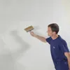 A man is applying a white substance to a wall with a brush. Produktbild-Vorschau