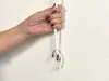 A hand holding a white cord with a metal ring and a weight attached to it, against a textured white wall. Voir les images du produit