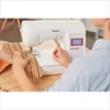 A person is using a Brother sewing machine to sew a patterned fabric. Produktbild-Vorschau