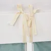 Close-up of ties on a white crib skirt with a green fabric underneath. Produktbild-Vorschau