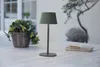 A table lamp sits on an outdoor table next to a basket of plants and a notebook with a pen. Produktbild-Vorschau