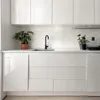 A clean, modern kitchen counter with white cabinets, a sink, and a faucet. Two potted plants add a touch of greenery. Produktbild-Vorschau