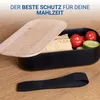 A black lunchbox with a wooden lid, filled with bread, tomatoes, and cucumber, sits on a wooden surface. A black elastic strap is placed in front of the lunchbox. Produktbild-Vorschau