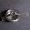 A close-up, angled view of a metal cookie press attachment on a dark gray surface. Produktbild-Vorschau
