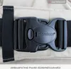 A close-up of a black buckle on a beige fabric strap, likely part of a baby carrier or backpack. Produktbild-Vorschau