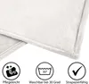 Close-up of a white fluffy blanket with icons and text indicating care instructions. Produktbild-Vorschau