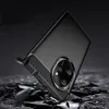 A black phone case with a carbon fiber pattern on the sides and a metallic ring around the camera module is shown at an angle, appearing to be falling onto a dark, rocky surface. Náhľad obrázku produktu