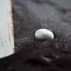 A close-up of a small gray stone resting on a dark, fluffy surface, possibly a rug. Produktbild-Vorschau