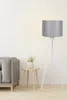 A floor lamp with a gray shade and white tripod base stands next to a gray sofa and a small wooden side table with a potted plant.