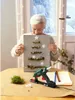 A woman is holding a handmade Christmas tree decoration while a hot glue gun and craft supplies are on the table. Produktbild-Vorschau