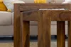 A close-up view of two wooden nesting tables in a living room setting, with a couch and decorative items in the background. Podgląd zdjęcia produktu
