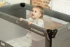 A baby is standing in a travel crib. Anteprima dell’immagine prodotto